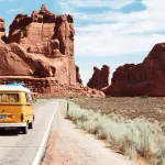 Yellow camper van on a desert road between red rock cliffs