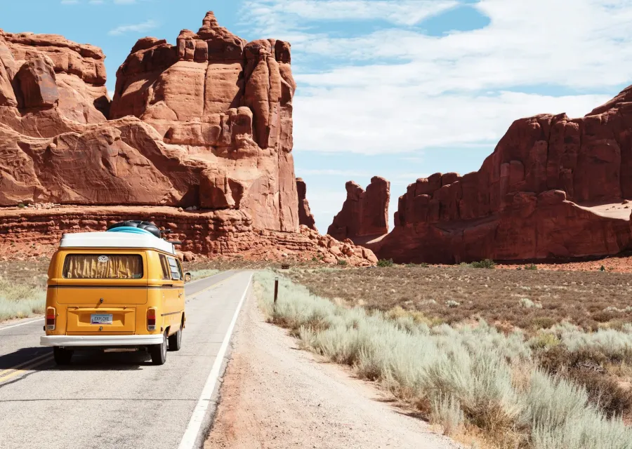 Yellow camper van on a desert road between red rock cliffs