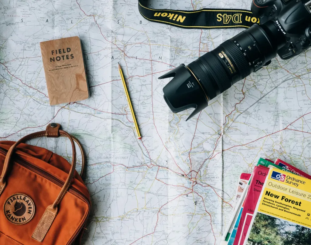 Paper map, camera, notebook and orange backpack on a table