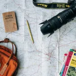 Paper map, camera, notebook and orange backpack on a table