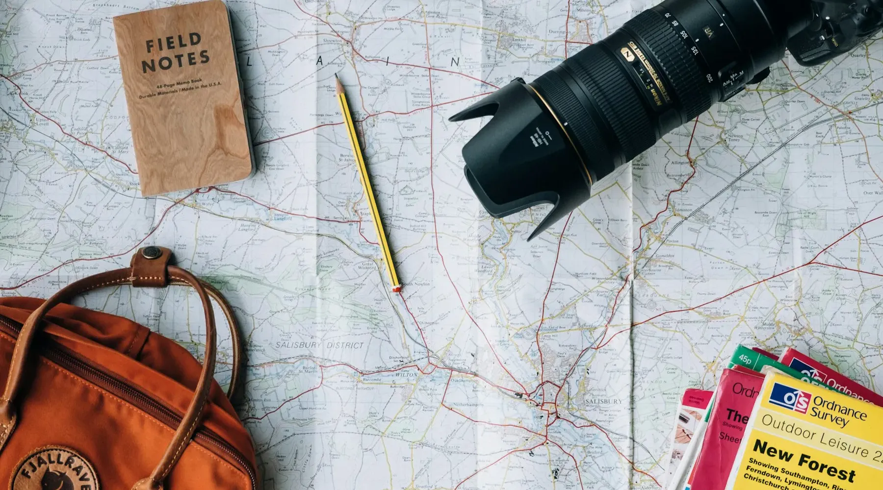 Paper map, camera, notebook and orange backpack on a table