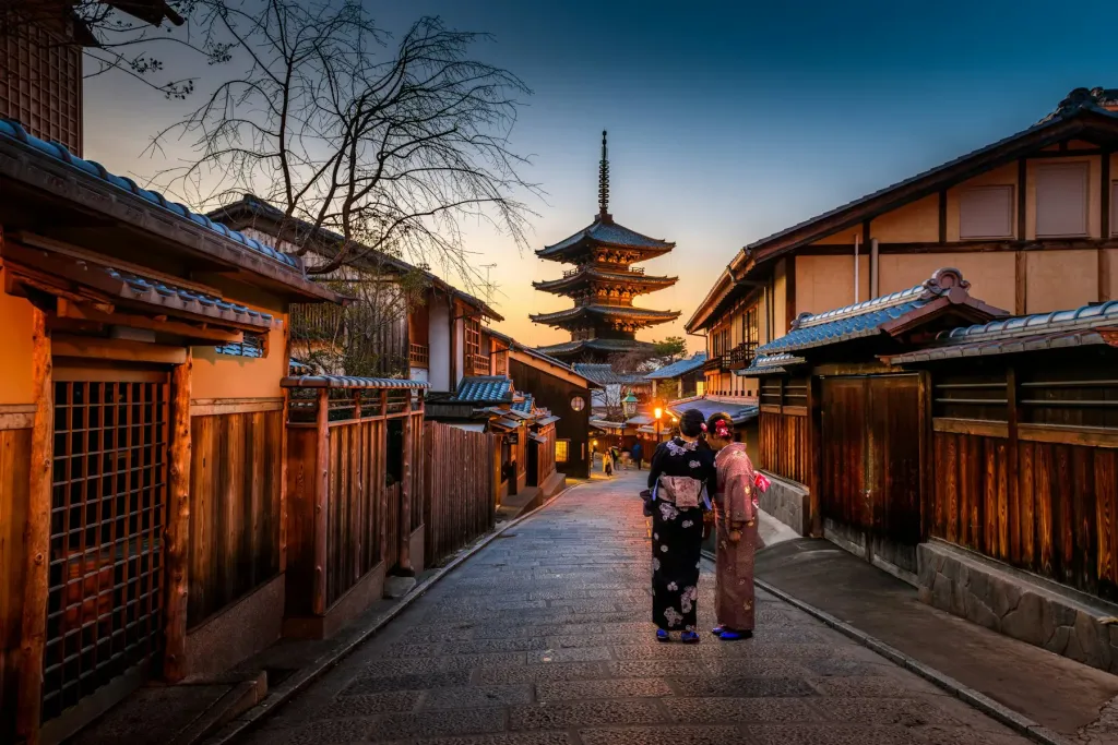 Woman in a kimono walking a lantern-lit Kyoto lane toward a pagoda