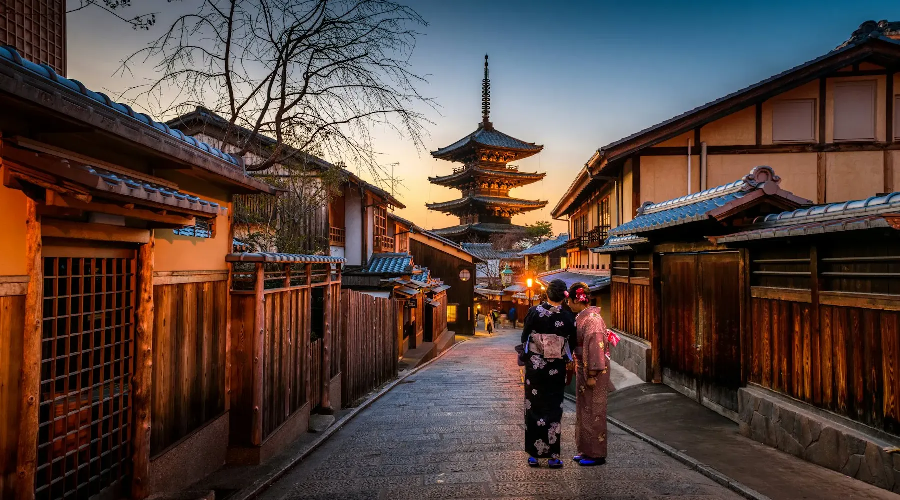 Woman in a kimono walking a lantern-lit Kyoto lane toward a pagoda