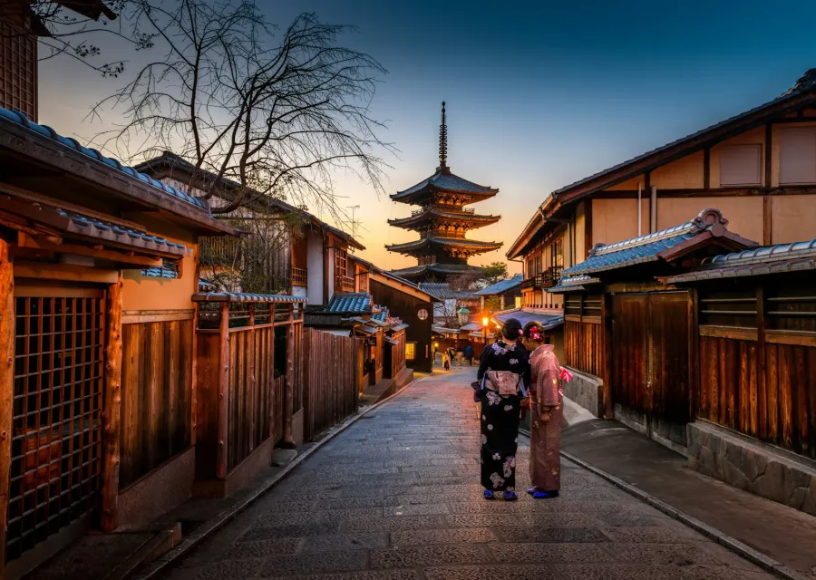 Woman in a kimono walking a lantern-lit Kyoto lane toward a pagoda