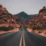 Straight two-lane highway leading toward red desert buttes
