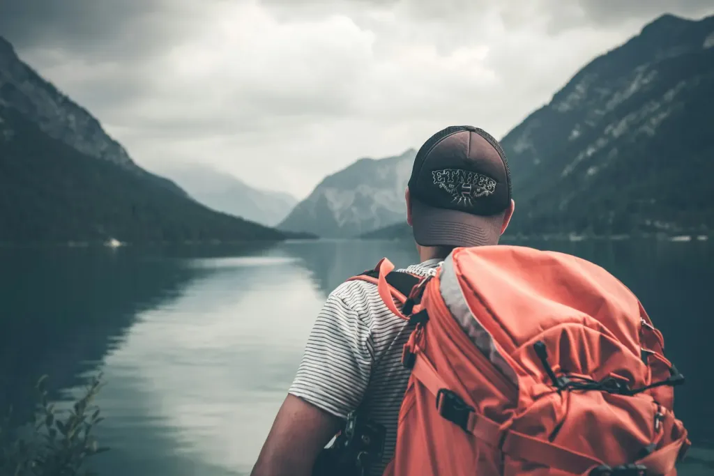 Hiker with an orange backpack looking at a lake between mountains