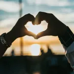 Hands making a heart shape against the setting sun