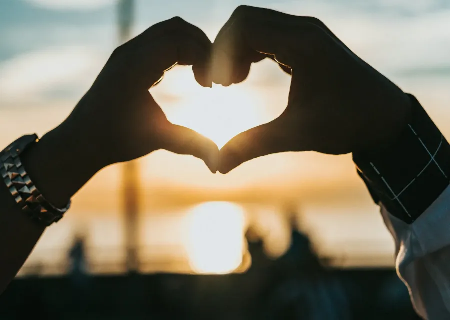 Hands making a heart shape against the setting sun