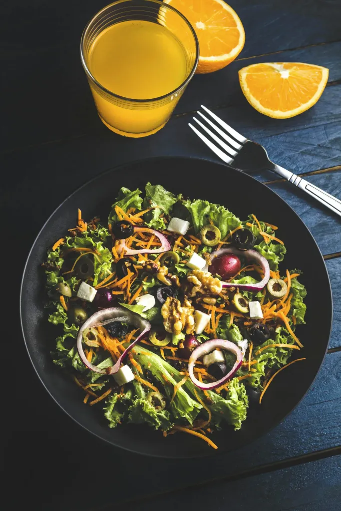 Salad with red onion on a dark plate beside orange juice