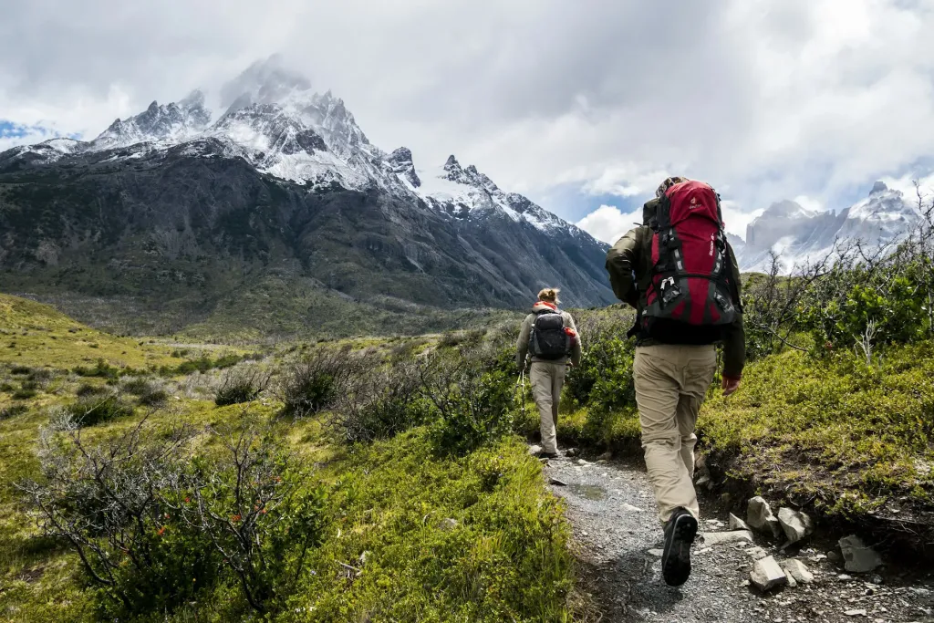 Two hikers with backpacks on a trail below snowy peaks