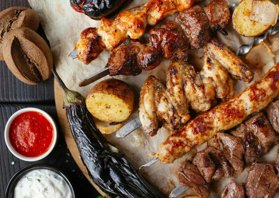Grilled kebabs, vegetables and dips on a dark table