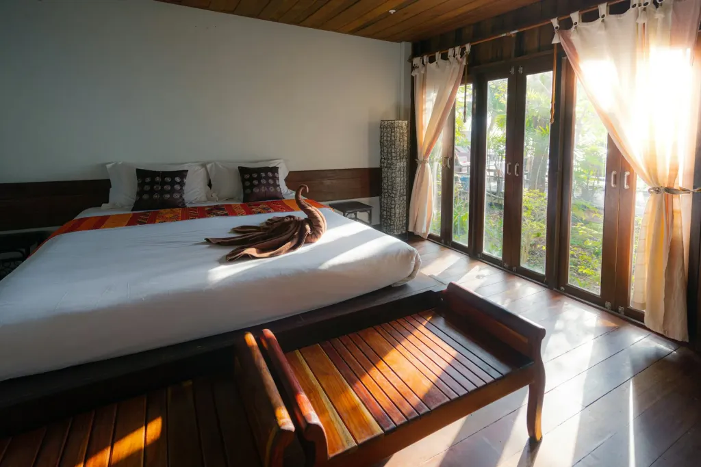 Hotel room with a wooden bed and tall windows to a garden